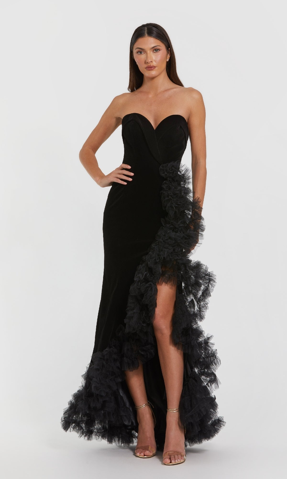 A woman in the Mac Duggal 68697 long formal dress—strapless velvet with a sweetheart neckline, thigh-high slit, and ruffled tulle trim—stands against a plain light background.